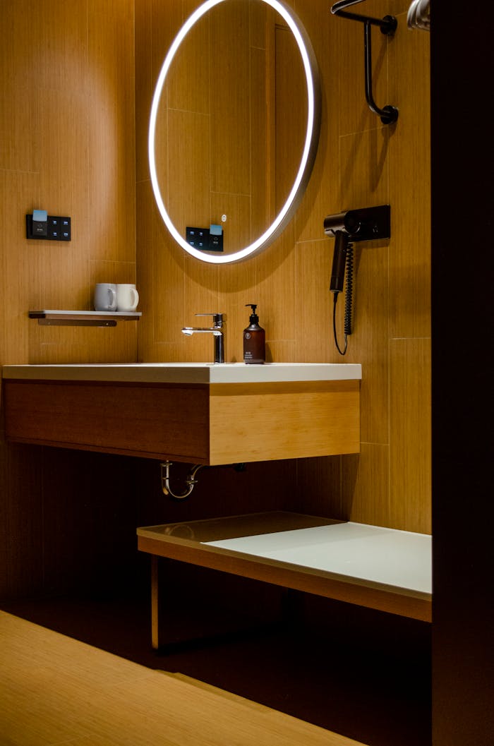services-02 Contemporary bathroom with wooden decor, illuminated mirror, and amenities.